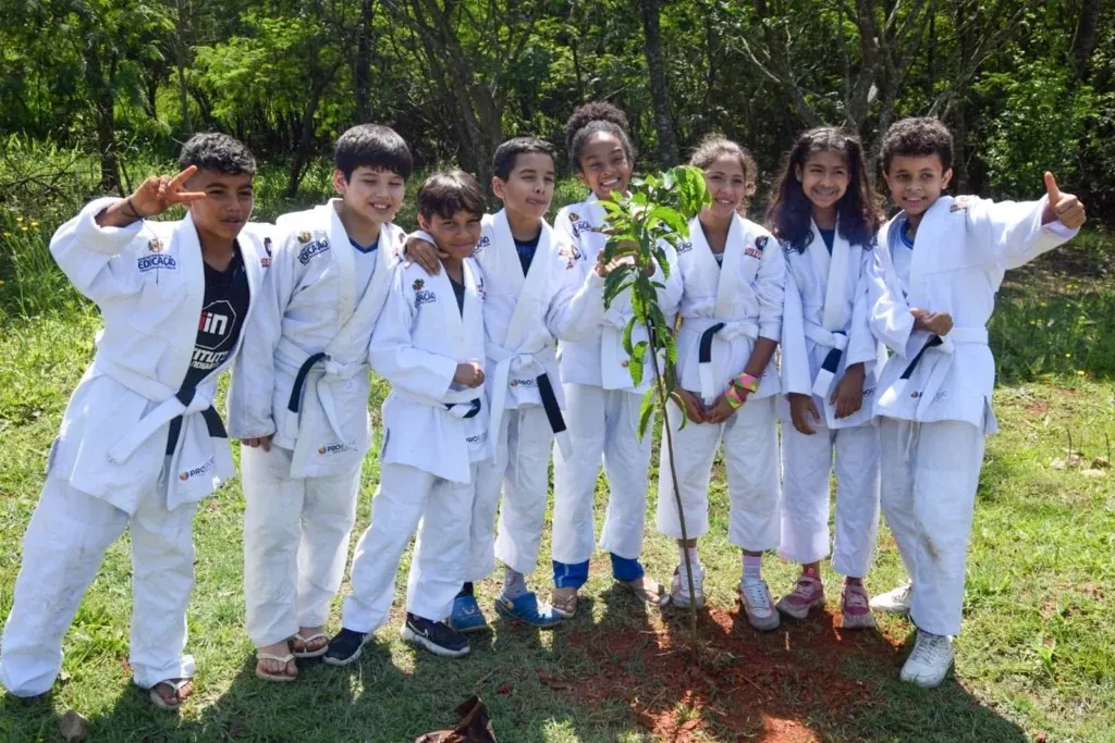 Crianças de quimono sorriem ao redor de uma muda recém-plantada no Parque Ecológico de Itaquaquecetuba