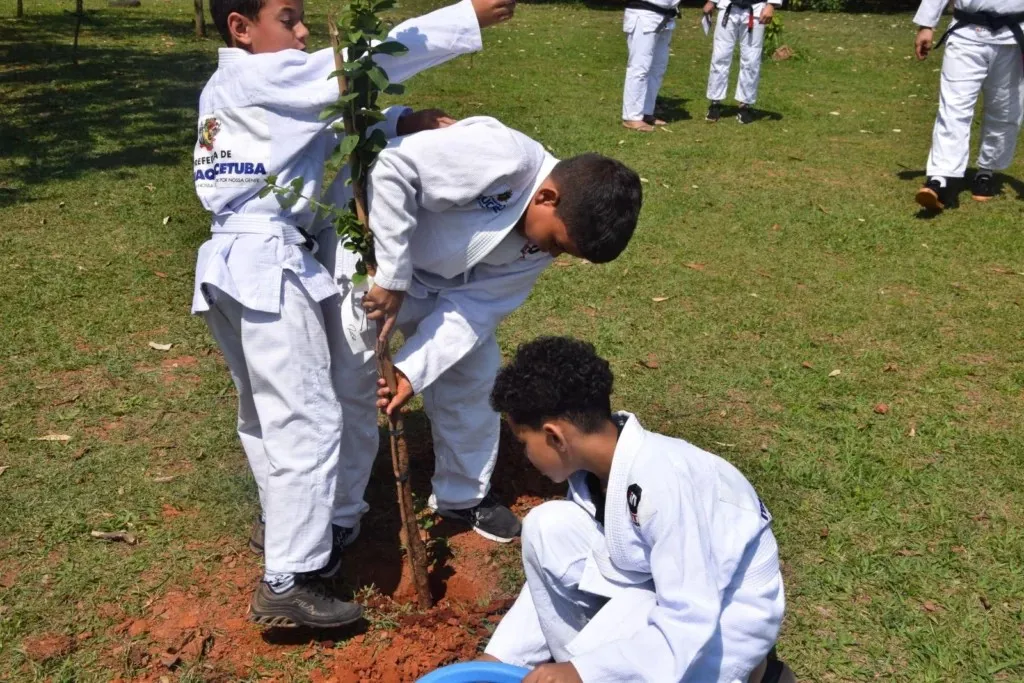 Alunos de quimono firmam a muda e preparam a terra durante o plantio