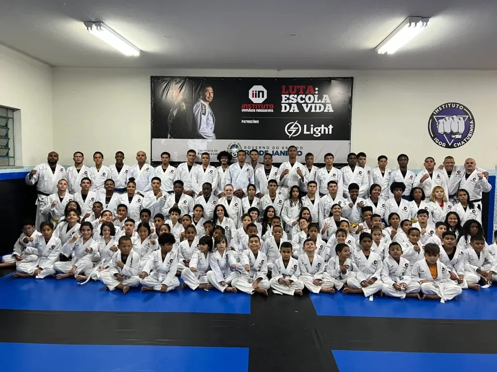 Turma de jiu-jitsu do Luta Escola da Vida, de quimono, reunida no tatame diante do banner do projeto