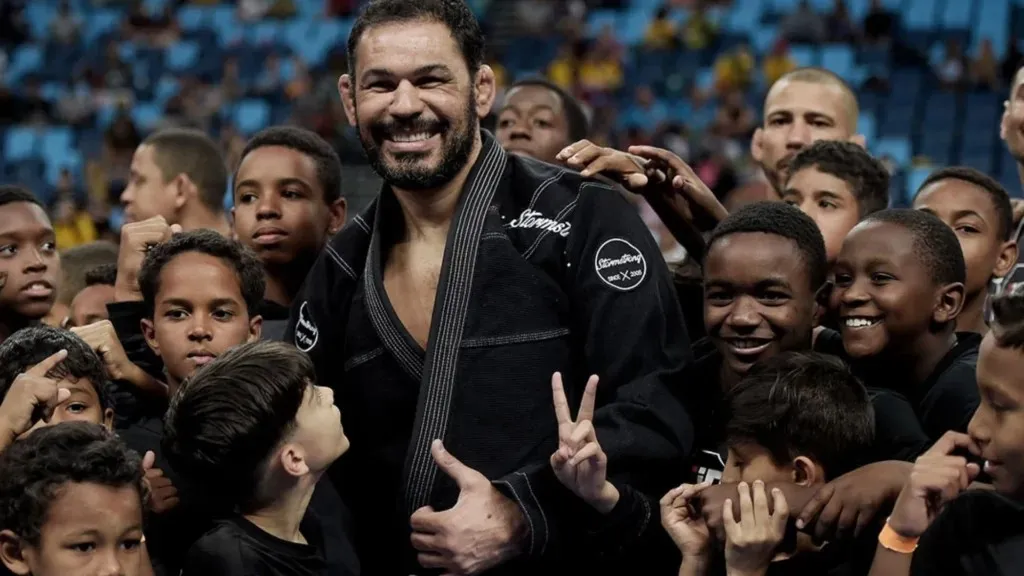 Rodrigo Minotauro sorrindo, cercado de crianças do Instituto em uma arena